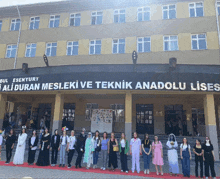 a group of people standing in front of a building that says " ali duran mesleki ve teknik anadolu lises "