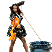 a woman in a black and orange dress is holding a mop over a trash can