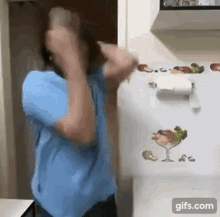 a man in a blue shirt is standing in front of a refrigerator with a paper towel holder on it .