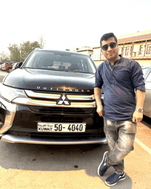 a man stands in front of a black outlander with a license plate that says kuwait 50-4040