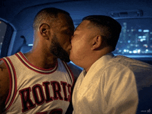 a man in a kolris jersey kisses another man in a white robe