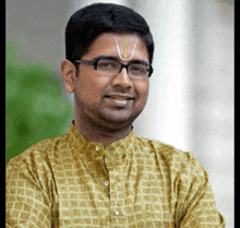 a man wearing glasses and a yellow shirt has a white circle on his forehead