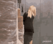 a woman in a black suit is standing in front of a wall with boxes on it .