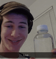 a man wearing a hat and headphones is holding a bottle of water with the word live written on it