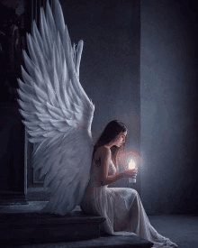 a woman with angel wings is sitting on a staircase holding a candle