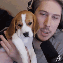 a man is holding a brown and white puppy in front of a microphone with the letter a on it