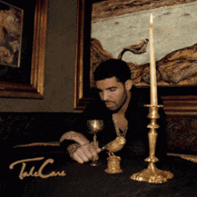 a man sits at a table with a candle and a candle holder with the word take care on the bottom