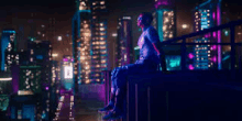 a man is sitting on a ledge overlooking a city at night .