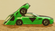 a green car with the hood up is sitting on a sandy surface