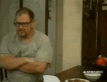 a man is sitting at a table with his arms crossed in front of a msnbc logo on the wall