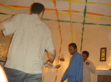 a man in a white shirt stands in a room with ribbons on the ceiling