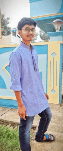 a young man wearing glasses and a blue shirt is standing in front of a blue and yellow wall