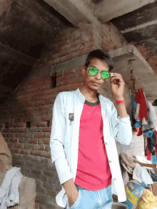 a young man wearing sunglasses stands in front of a brick wall with clothes hanging on it