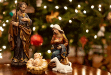 a nativity scene with a baby in a manger and a sheep in front of a christmas tree