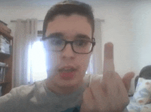 a young man wearing glasses is making a middle finger sign .