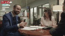 a man in a suit sits at a table with a woman and a sign that says lopez tv land on it