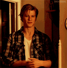 a young man wearing a plaid shirt and a white t-shirt is smiling