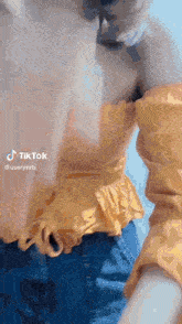 a woman in a yellow off the shoulder top and blue jeans is standing in front of a blue sky .