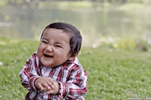 a baby in a plaid shirt is laughing in the grass ..