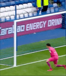 a soccer player in a pink jersey is about to kick a ball in front of an energy drink sign