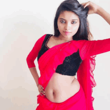 a woman in a red saree and a black blouse is standing in front of a white wall .