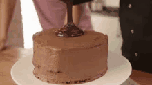 a chocolate cake is being decorated with chocolate frosting on a white plate .