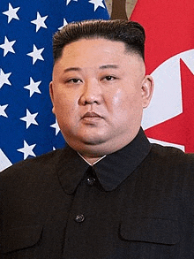 a man in a black suit is standing in front of an american flag and a korean flag .