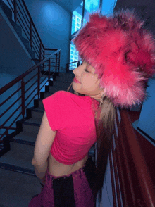 a woman wearing a pink top and a pink hat stands on a set of stairs