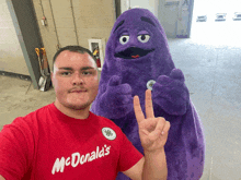 a man in a red mcdonald 's shirt poses with a purple stuffed animal