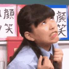 a girl in a school uniform is making a funny face in front of a chalkboard with chinese writing on it .