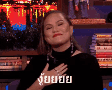 a woman in a black top is making a funny face with her hand on her chest in front of bookshelves