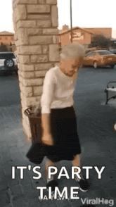 an elderly woman is dancing in front of a brick wall and says `` it 's party time '' .