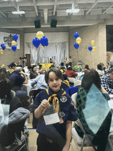 a boy scout stands in front of a crowd in a room with a banner that says ' chris ' on it