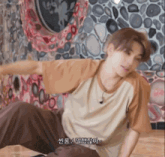 a man in a tan shirt is dancing in front of a wall with rocks on it