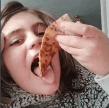 a young girl is eating a piece of pizza with her tongue out