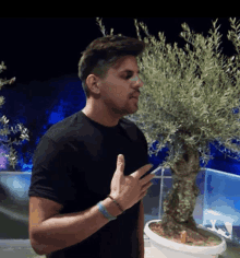 a man in a black shirt stands in front of a potted plant