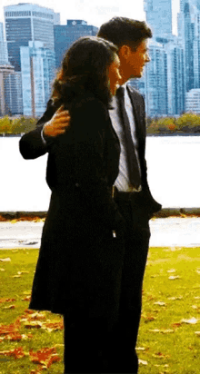 a man in a suit and tie is hugging a woman in a black coat in front of a city skyline .