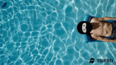 a man is laying on a raft in a pool with a tokeo logo on the bottom