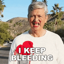 an elderly woman with blood on her face is wearing a white sweater that says " i keep bleeding "