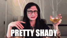 a woman with glasses is holding a glass of wine and saying `` pretty shady '' .