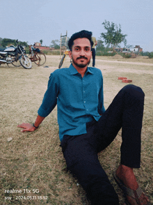 a man in a blue shirt is sitting in the grass with a realme 11x 5g phone behind him