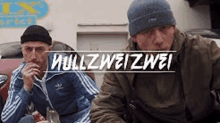 two men are sitting next to each other in front of a sign that says mullzweizwei