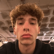 a young man with curly hair is taking a selfie in a room with a ceiling .