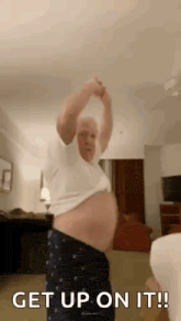 an older man is dancing in a living room while holding his arms up .
