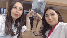 two women making a heart shape with their hands in front of a photo of a man