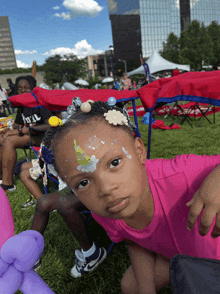 a little girl wearing a pink shirt is sitting in the grass with balloons in her hair