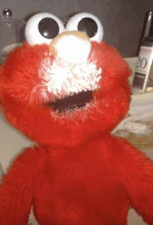 elmo stuffed animal with white powder on his face in front of a bottle of 20