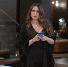 a woman in a black dress is holding a cell phone in her hands