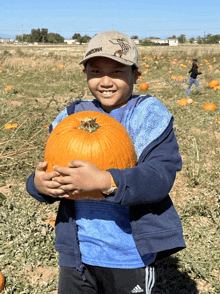 a boy wearing a arizona hat holds a pumpkin