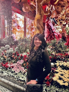 a woman in a black dress stands in front of a display of flowers and coins